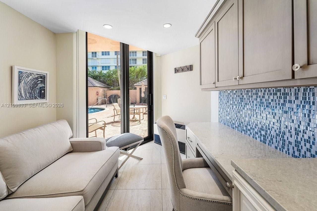 Built-in cabinetry with stone-finish countertops, mosaic tile backsplash, recessed ceiling lighting, and tile flooring, featuring sliding glass doors with access to an exterior patio area