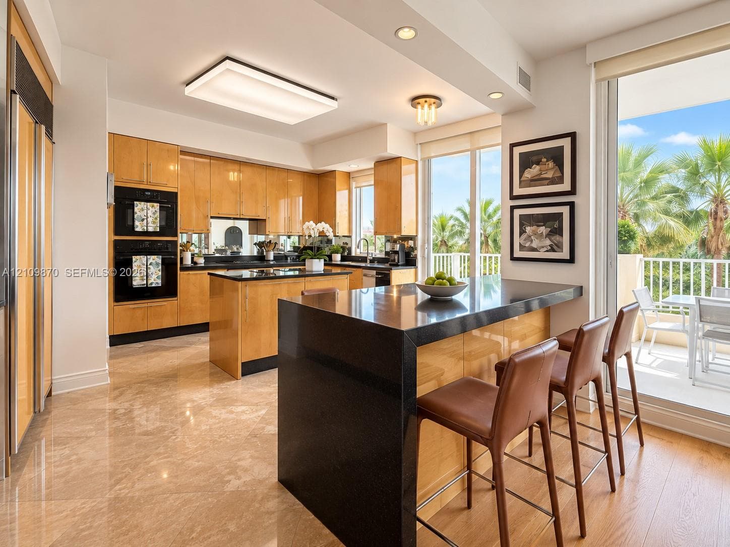 Kitchen featuring flat-panel wood cabinetry, black stone countertops, a central island with a waterfall edge, built-in double ovens, and large-format tile flooring