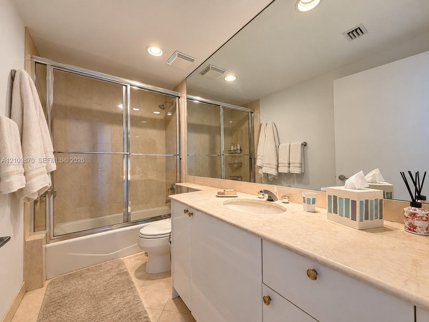 Full-width vanity with a stone countertop and integrated oval sink, floor-to-ceiling mirror, and shower-tub combination with a glass sliding enclosure