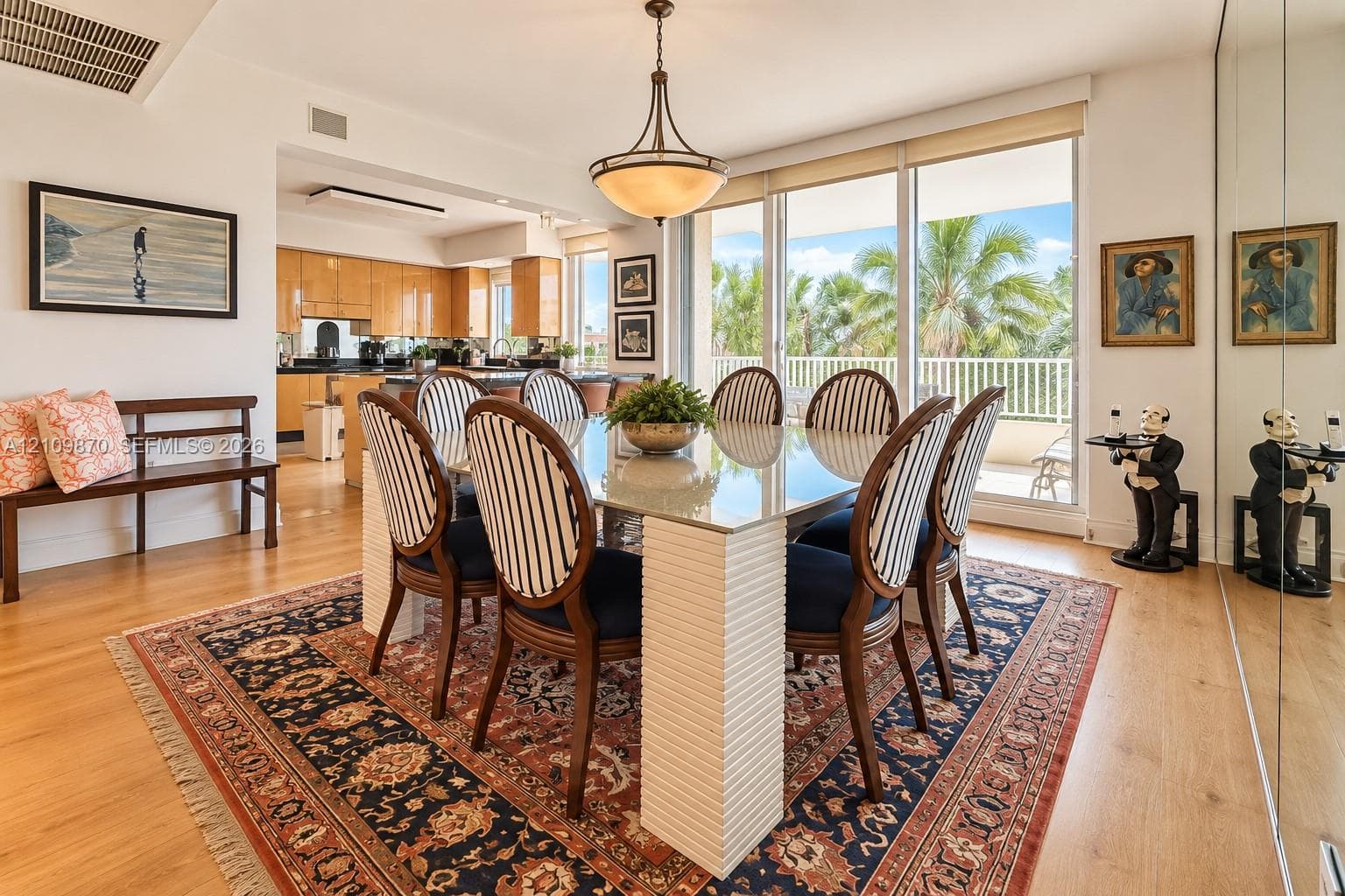 Dining area featuring wood-finish flooring, a tiered semi-flush mount light fixture, full-height mirrored wall paneling, and sliding glass doors with exterior access