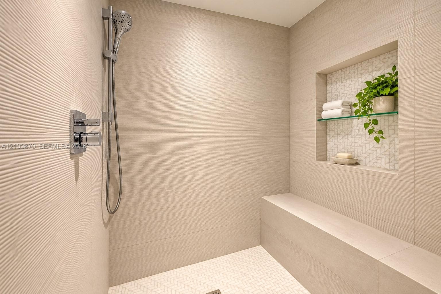 Walk-in shower featuring textured wall tile, a built-in stone bench, a recessed wall niche with glass shelving, and a multi-function handheld shower head