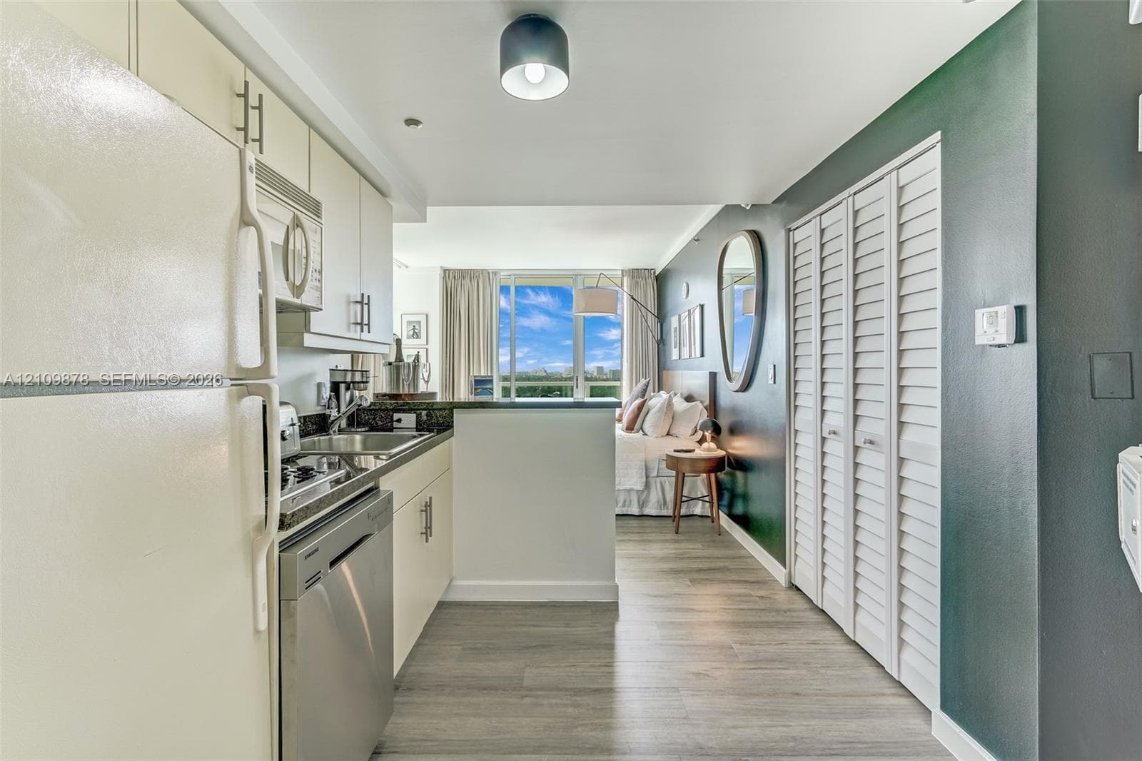 Kitchen area featuring wood-finish flooring, white cabinetry with silver-tone hardware, stainless steel dishwasher, and louvered closet doors