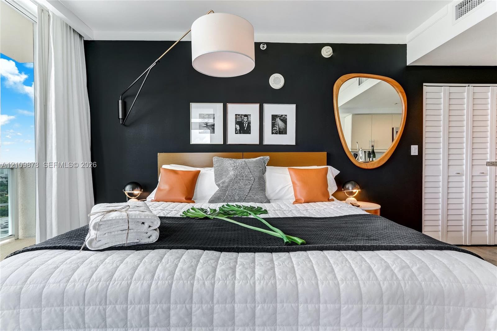 Accent wall featuring a matte black finish, oversized drum pendant lighting, asymmetric wall-mounted mirror, and louvered double-door closet