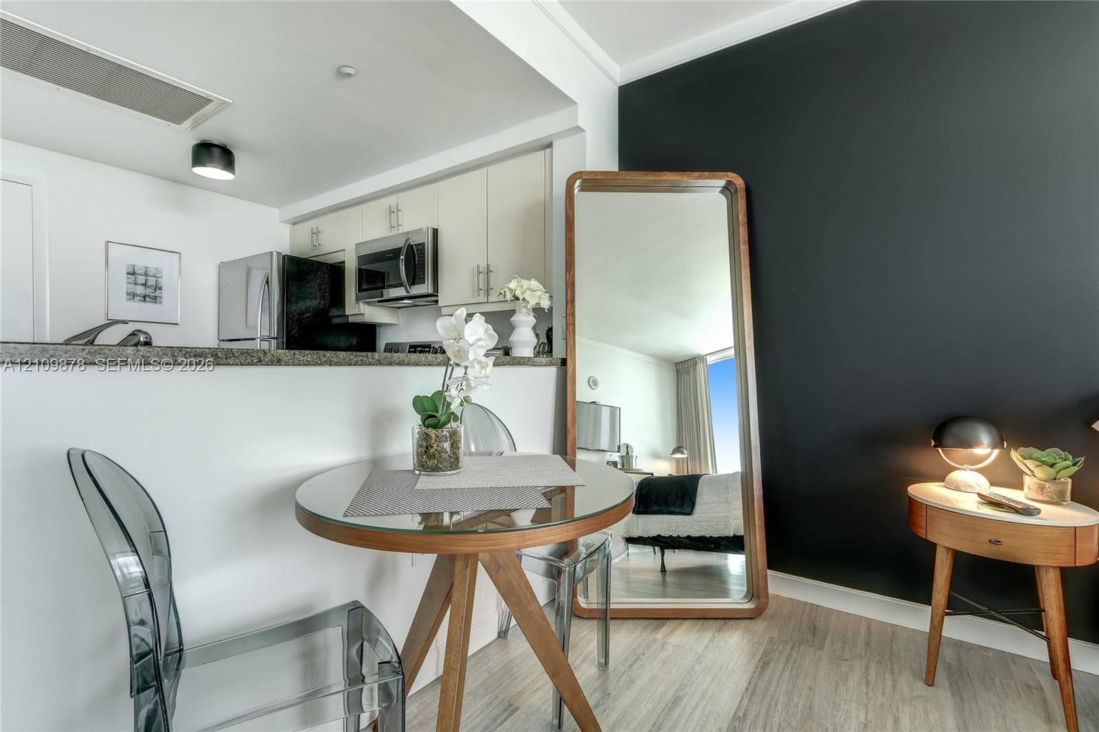 Kitchen featuring light-toned cabinetry, stainless steel microwave, stone-surface breakfast bar, and wood-finish flooring