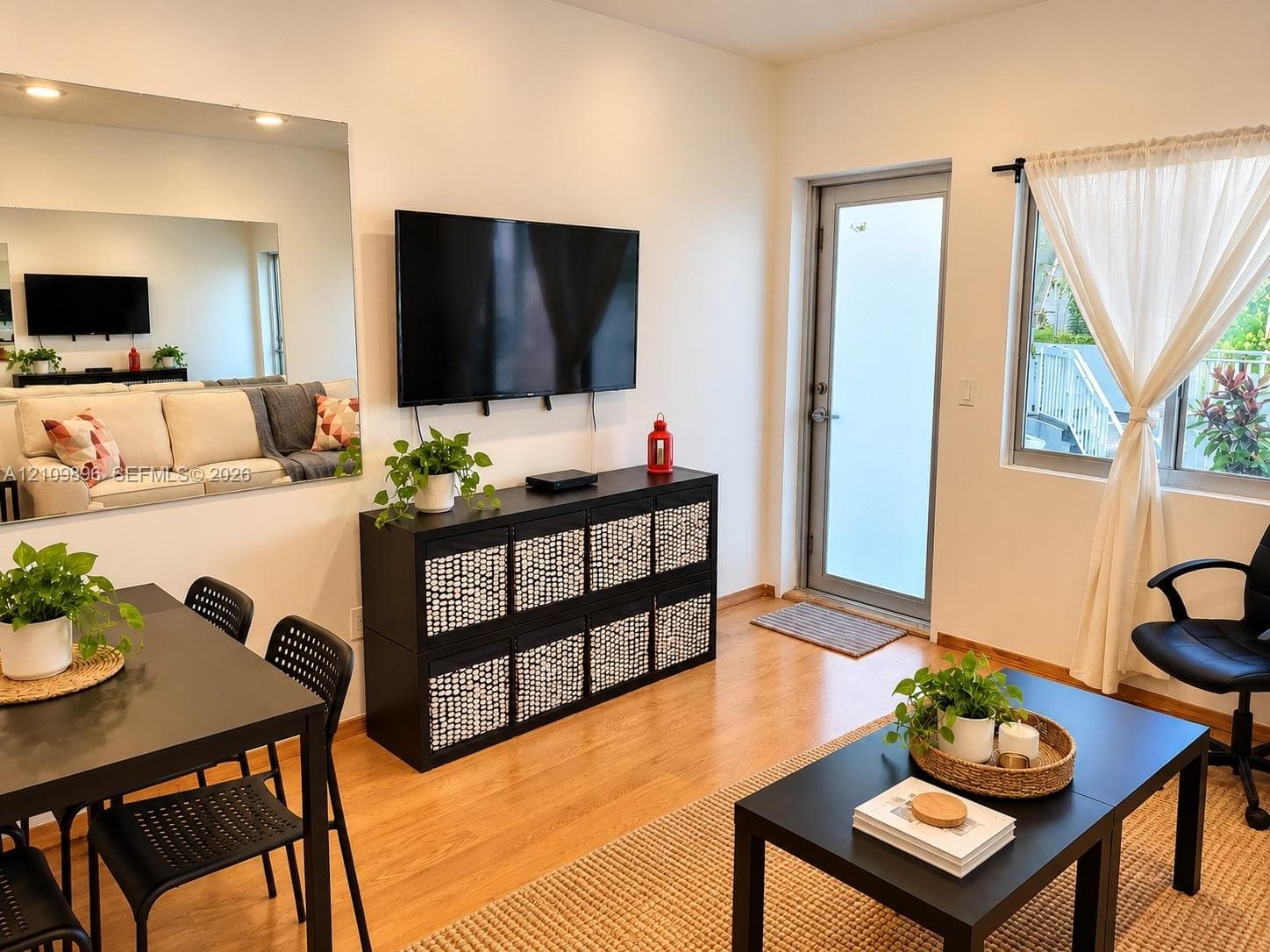 Living area featuring wood-finish flooring, a wall-mounted glass mirror, a glass-paneled exterior door, and recessed lighting