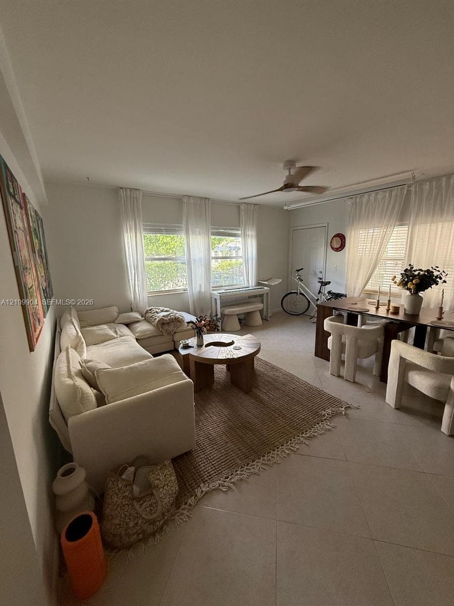 Living area featuring large-format tile flooring, multiple windows, and a ceiling fan