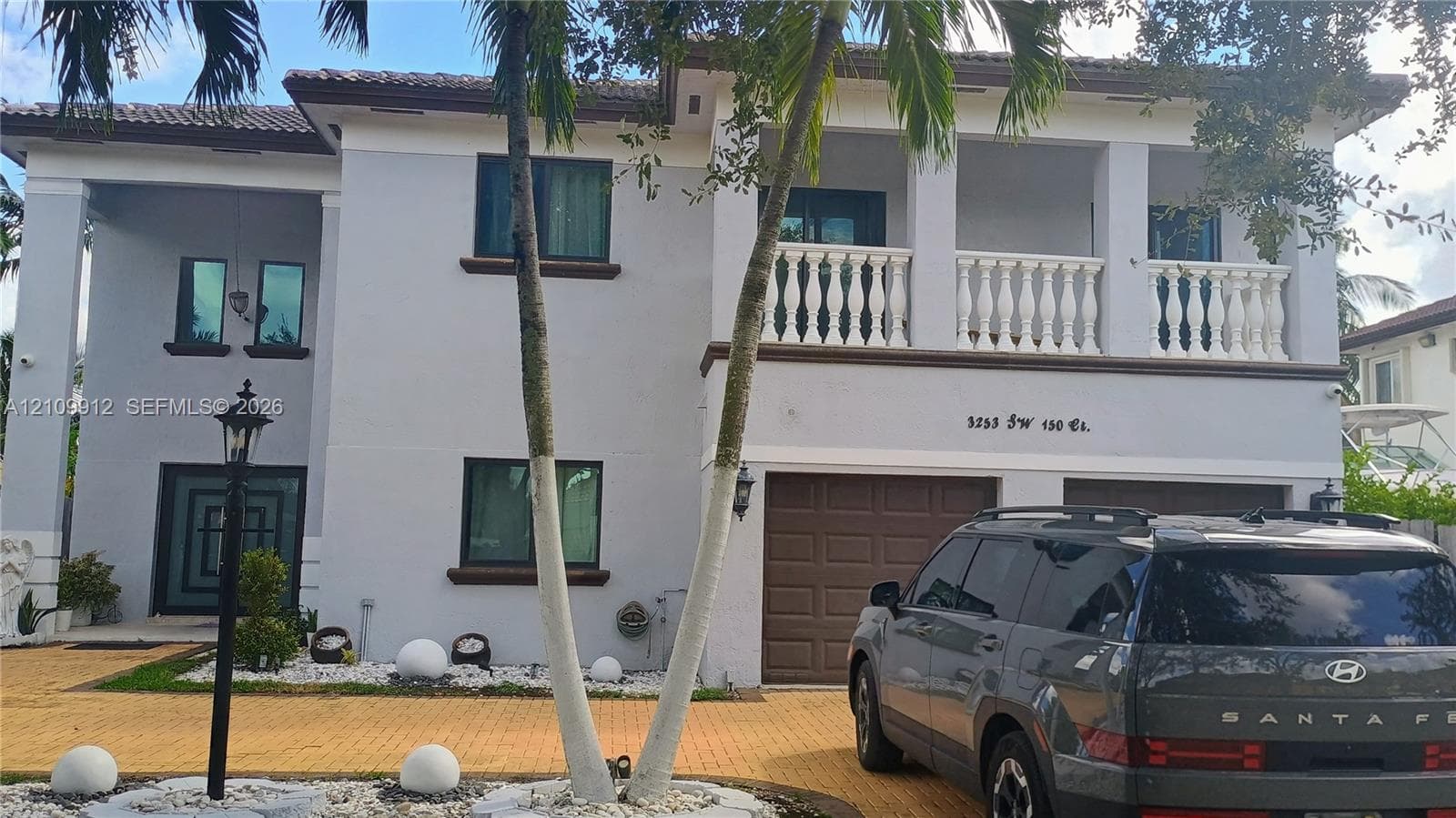 Two-story residence featuring a paved driveway, a second-floor balcony with balustrade railing, a tiled roof, and a two-car garage