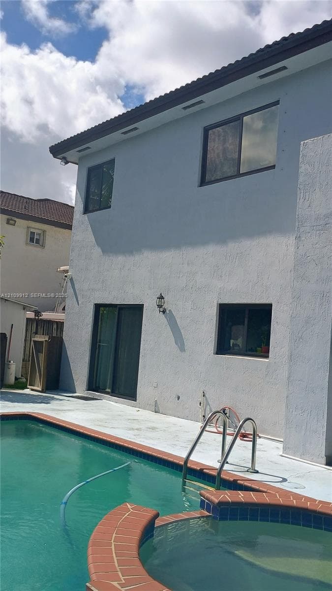 Exterior featuring a two-story stucco facade, private swimming pool, integrated spa, and concrete pool deck