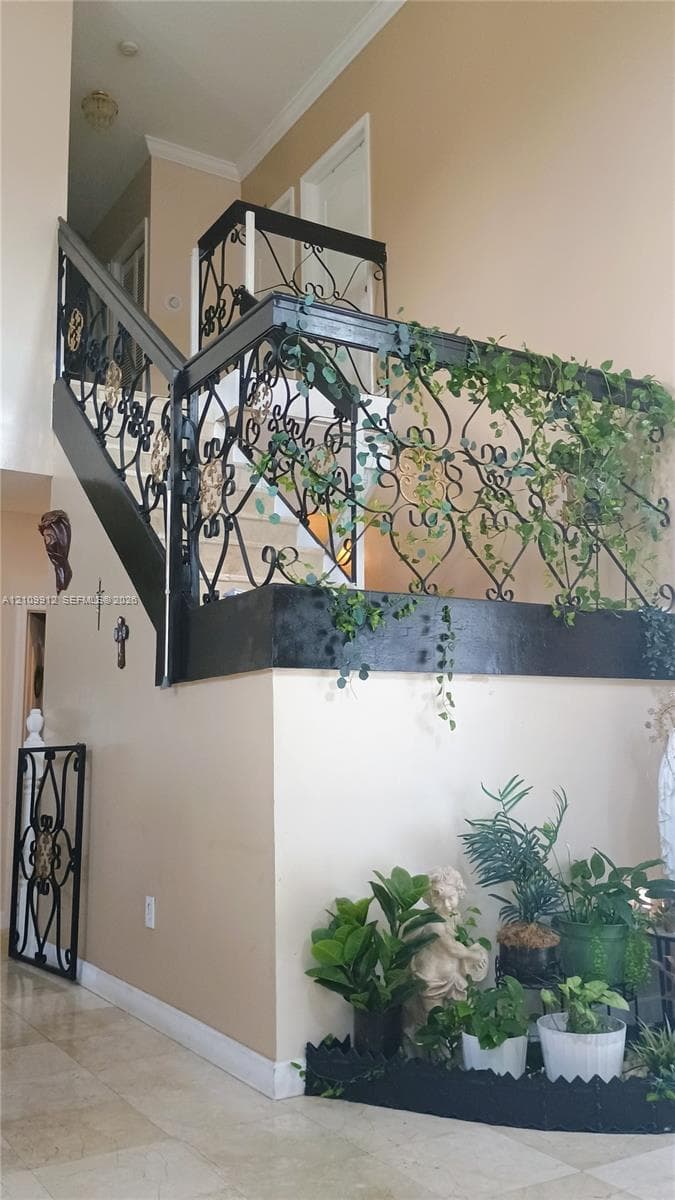 Staircase featuring decorative wrought-iron railings, high ceilings, and stone-finish tile flooring