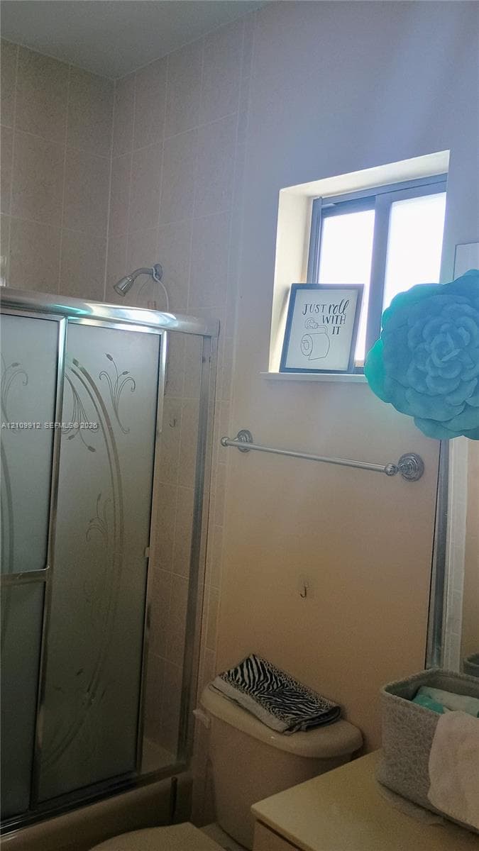 Shower enclosure featuring sliding glass doors with etched floral patterns and tile wall surround, complemented by a horizontal metal towel bar and a recessed window