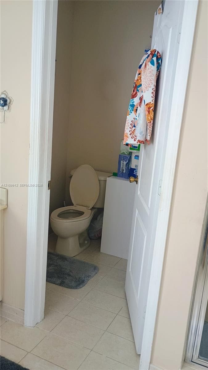 Enclosed water closet featuring tile flooring and a standard white commode