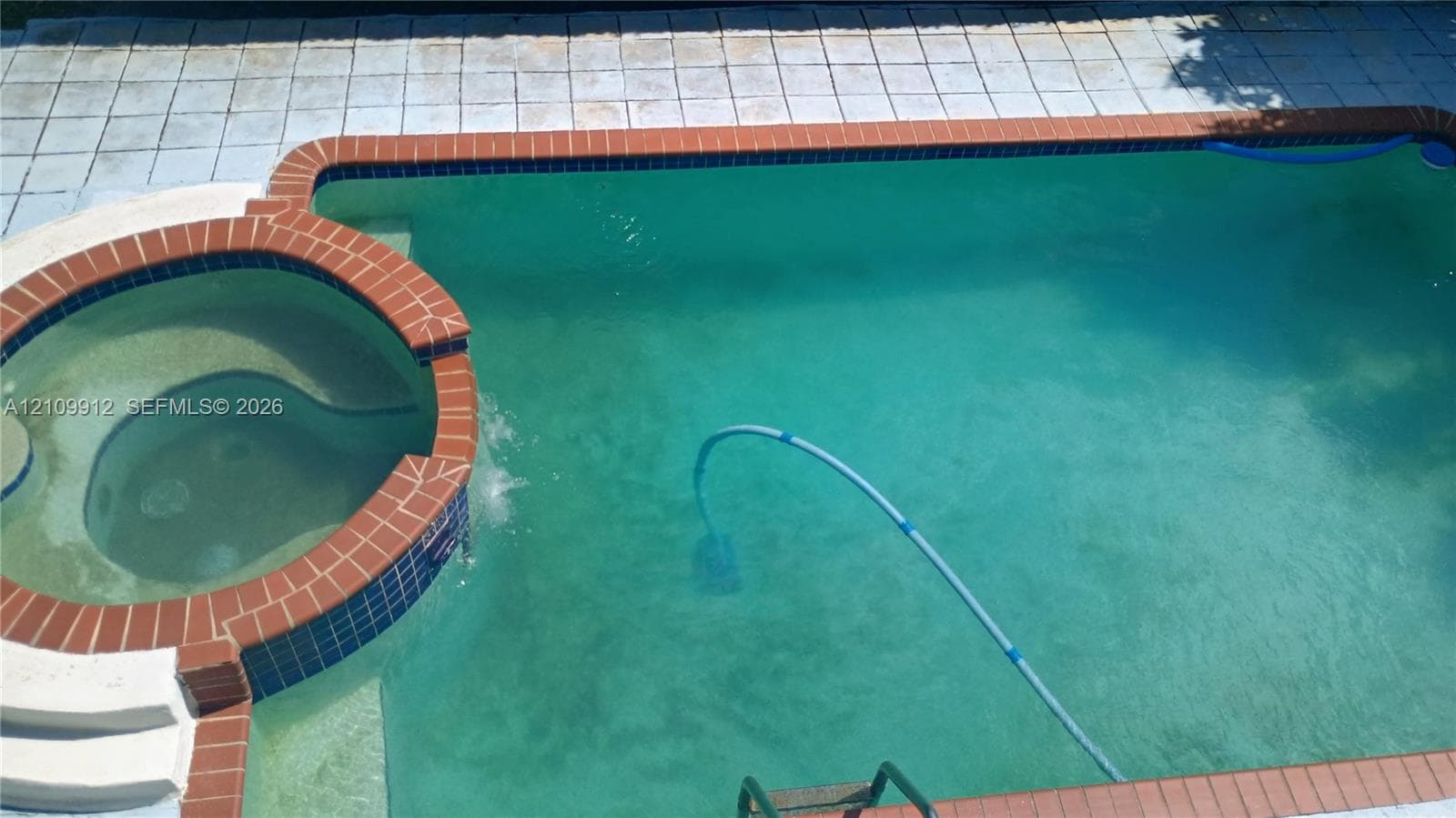 In-ground swimming pool with an integrated circular spa, brick coping, and light-toned patio hardscaping