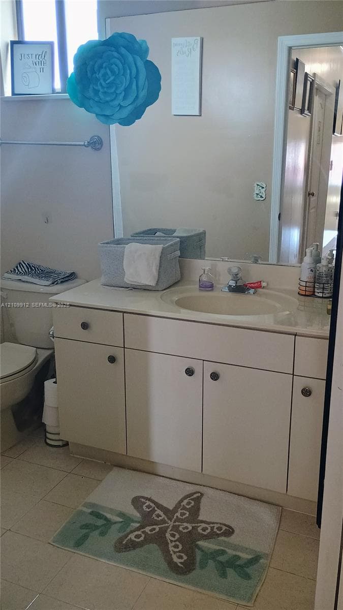Vanity with integrated sink and countertop, full-width wall mirror, and neutral tile flooring