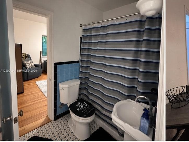Bathroom featuring blue and black wall tile accents, geometric patterned tile flooring, a pedestal sink with a curved faucet, and a porcelain toilet