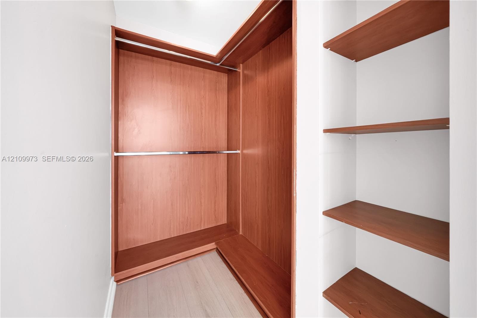 Built-in closet featuring wood-finish shelving, an L-shaped hanging rod system, and neutral wood-finish flooring