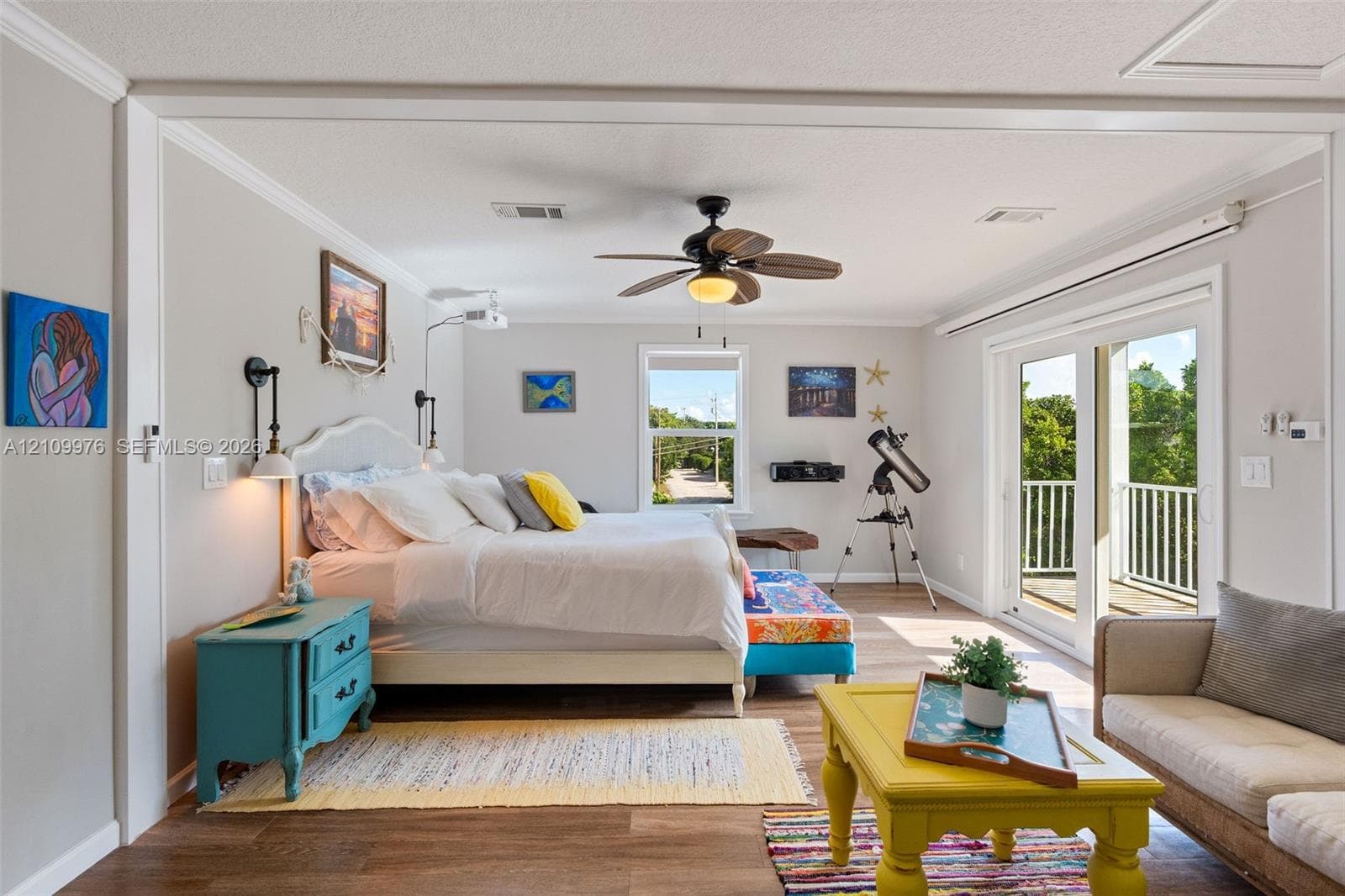 Living space featuring wood-finish flooring, a ceiling fan with integrated lighting, wall-mounted light fixtures, and glass sliding doors providing access to an exterior balcony