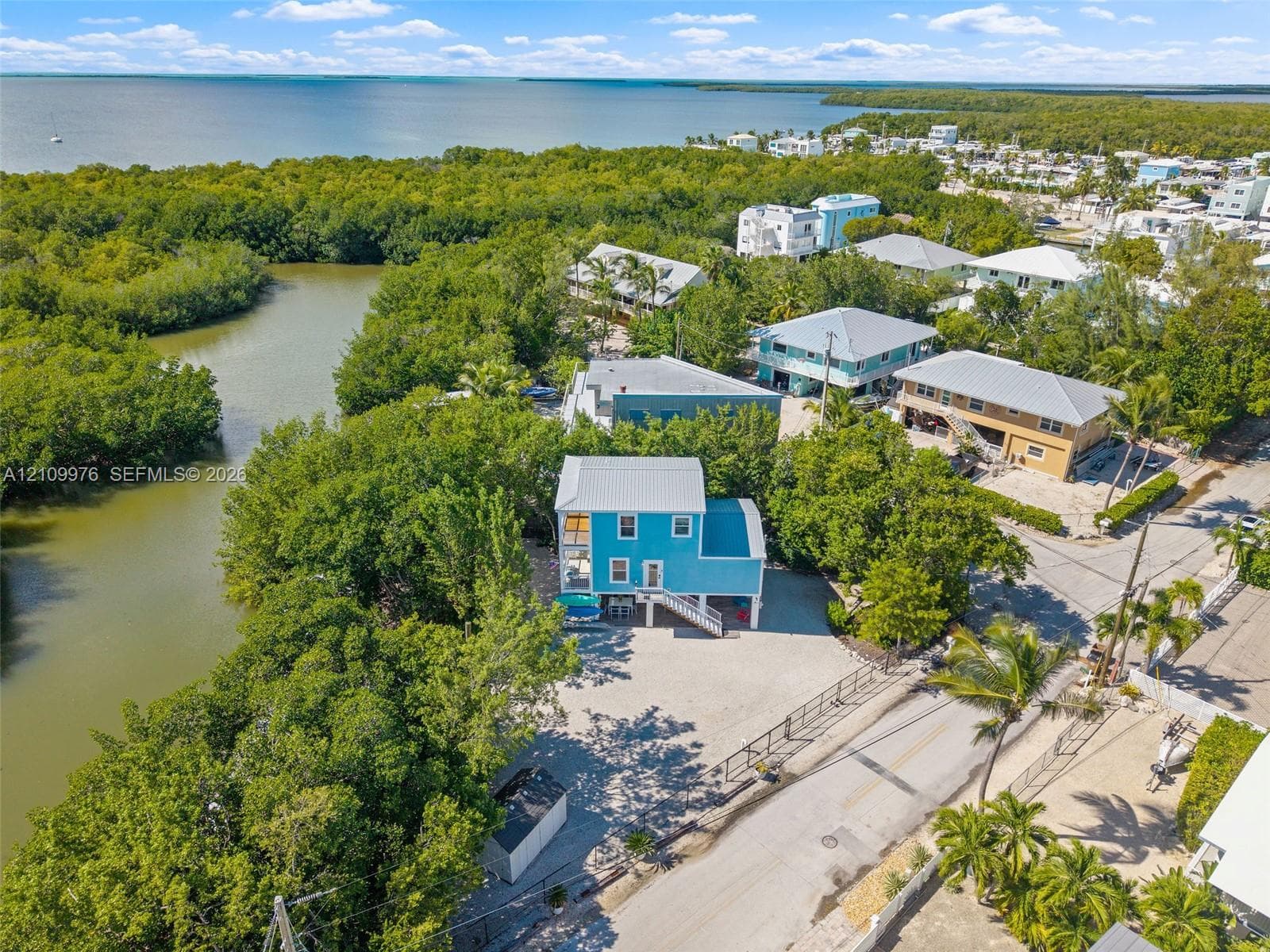Elevated residence featuring a metal roof, light-toned gravel lot, and waterfront positioning along a natural canal