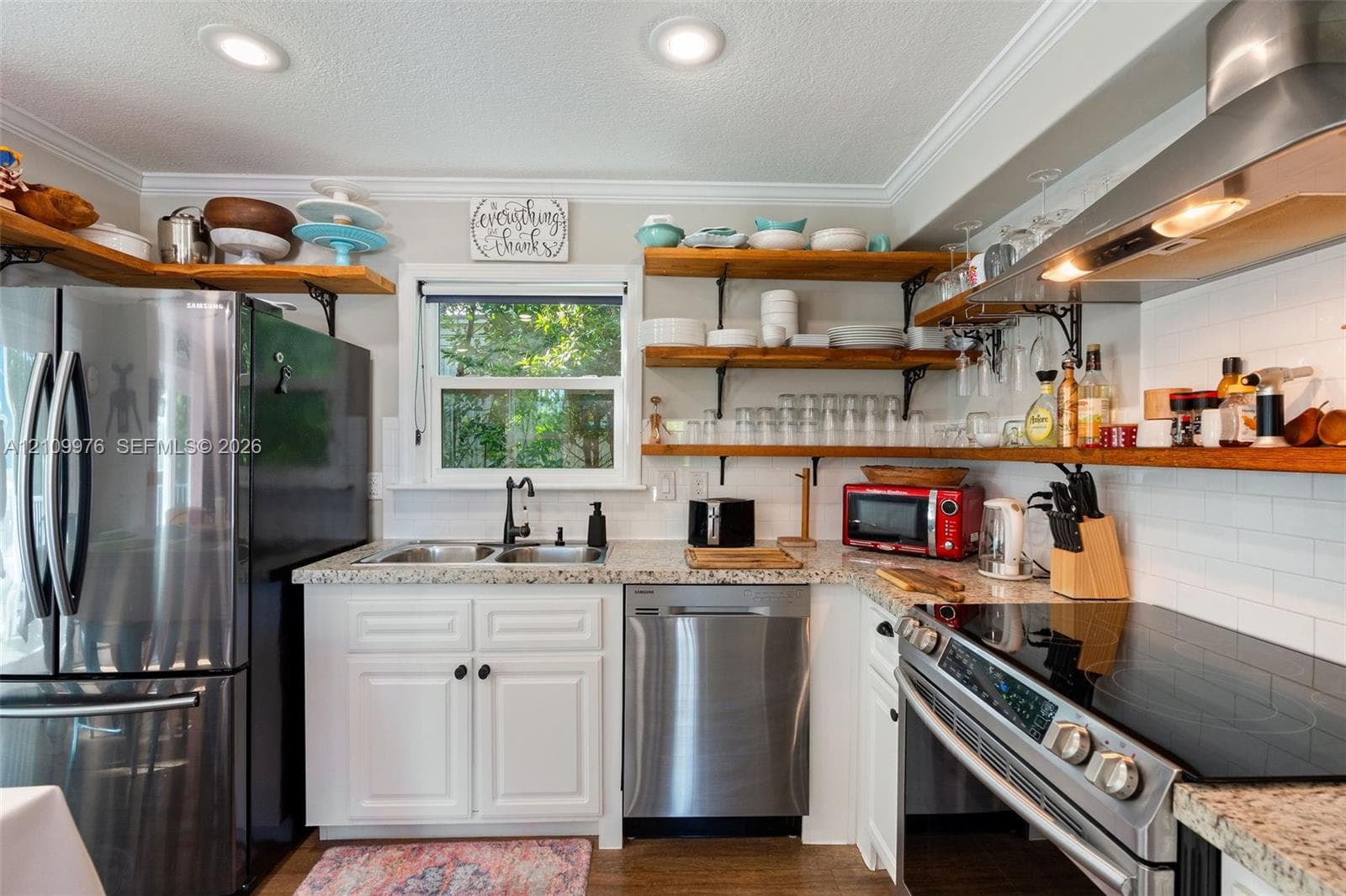 Kitchen featuring stainless steel appliances, speckled stone countertops, white cabinetry, open wood shelving, and a glass-tiled backsplash