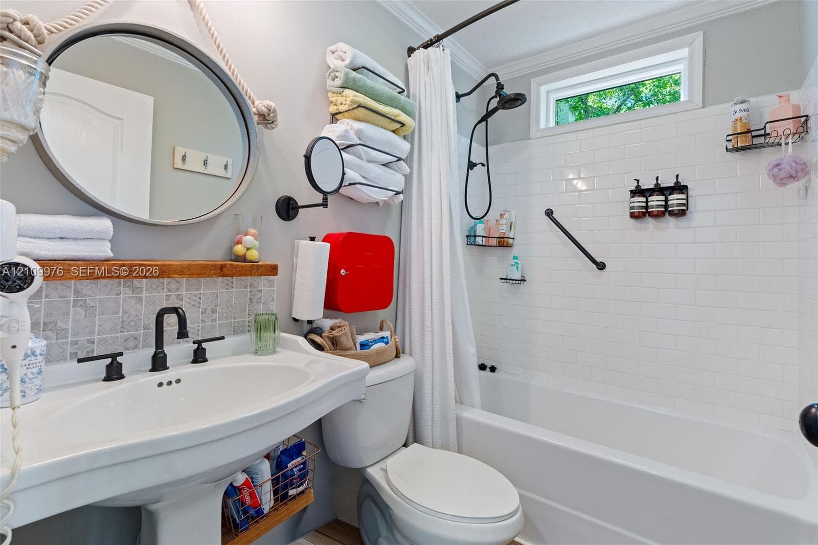 Bright, updated bathroom featuring a curved pedestal sink with matte black fixtures, subway tile shower surround with glass enclosure, circular mirror with black frame, and white subway tile backsplash above the vanity