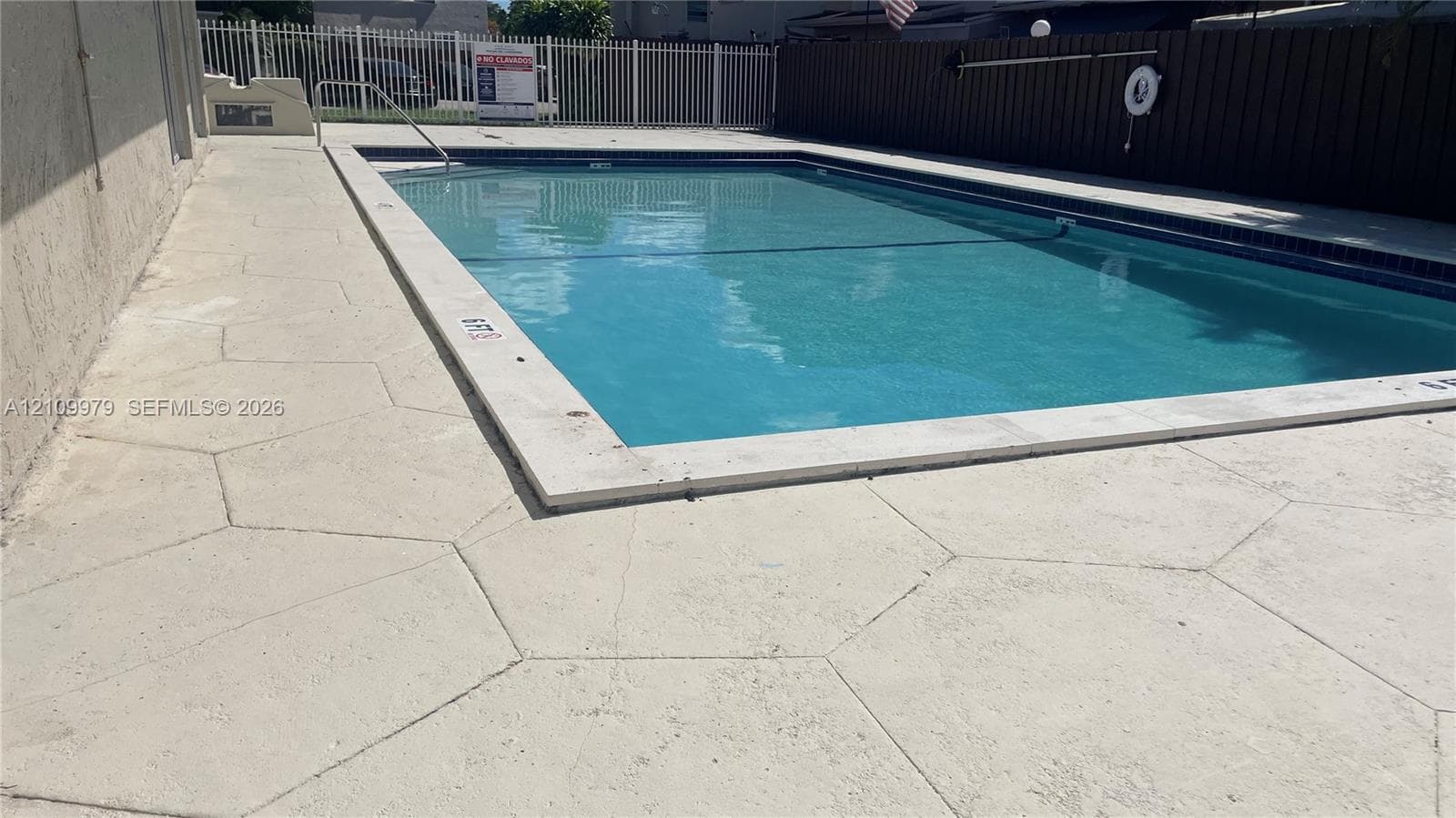 In-ground swimming pool featuring a concrete deck with hexagonal pattern pavers, metal perimeter fencing, and privacy screening
