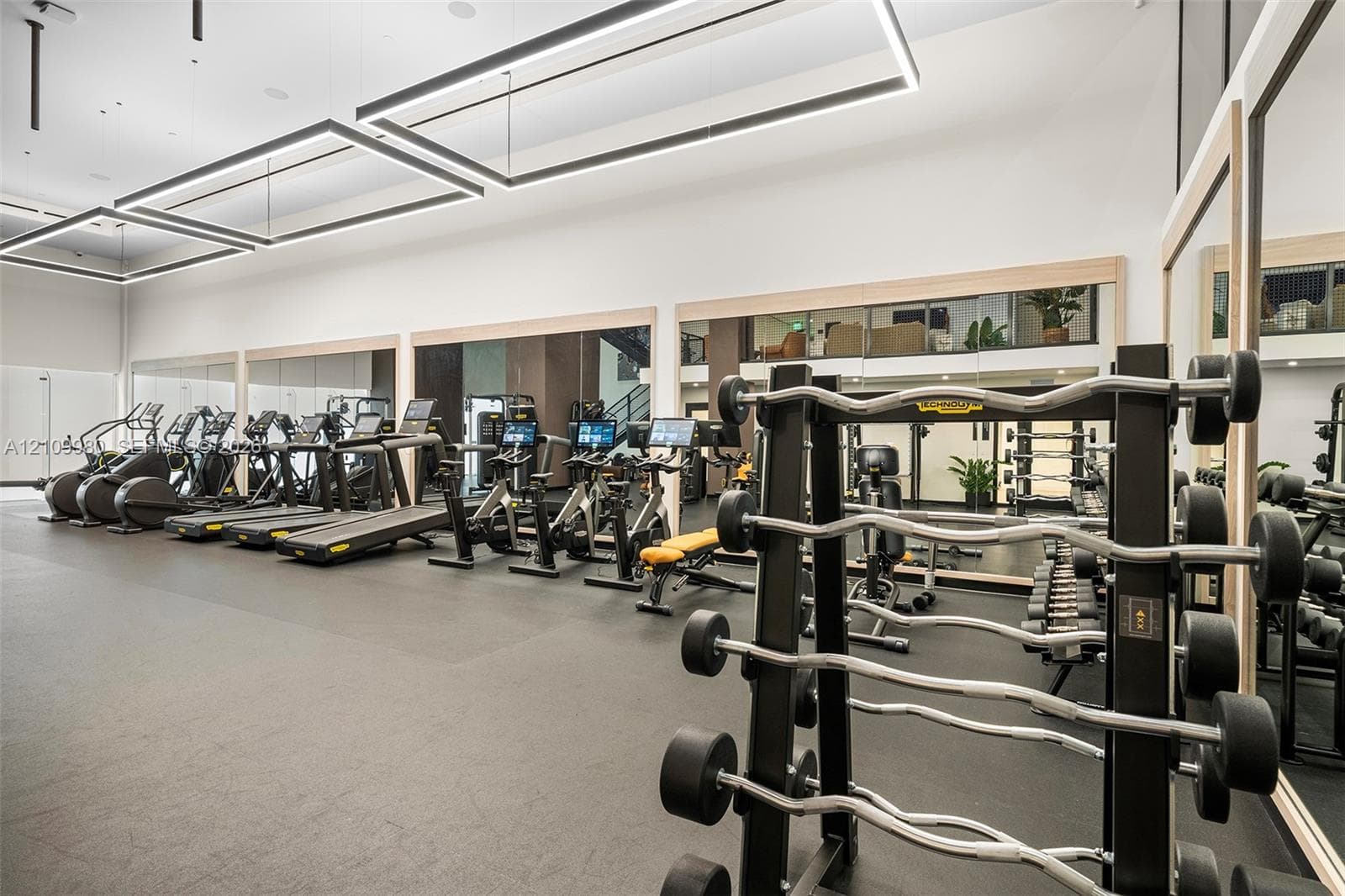 Fitness facility featuring high ceilings, rectangular modern pendant lighting, expansive wall-to-wall mirrors, and durable flooring