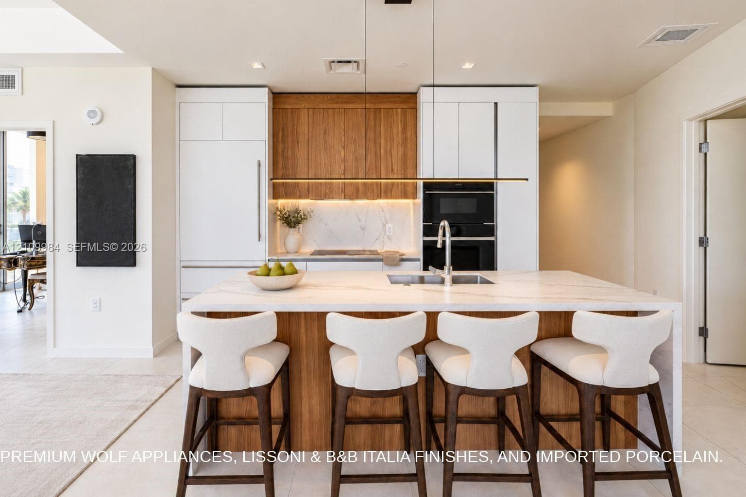 Kitchen featuring an expansive center island with a stone-finish countertop, integrated built-in appliances, flat-panel cabinetry in white and natural wood finishes, and under-cabinet LED task lighting