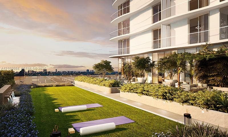 Landscaped rooftop terrace featuring synthetic turf, built-in stone planters with mature trees, glass perimeter railings, and a wall-mounted water feature