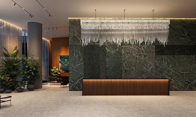 Lobby featuring a stone-clad accent wall, linear crystal chandelier, integrated under-cabinet lighting, wood-panel reception desk, and recessed track lighting