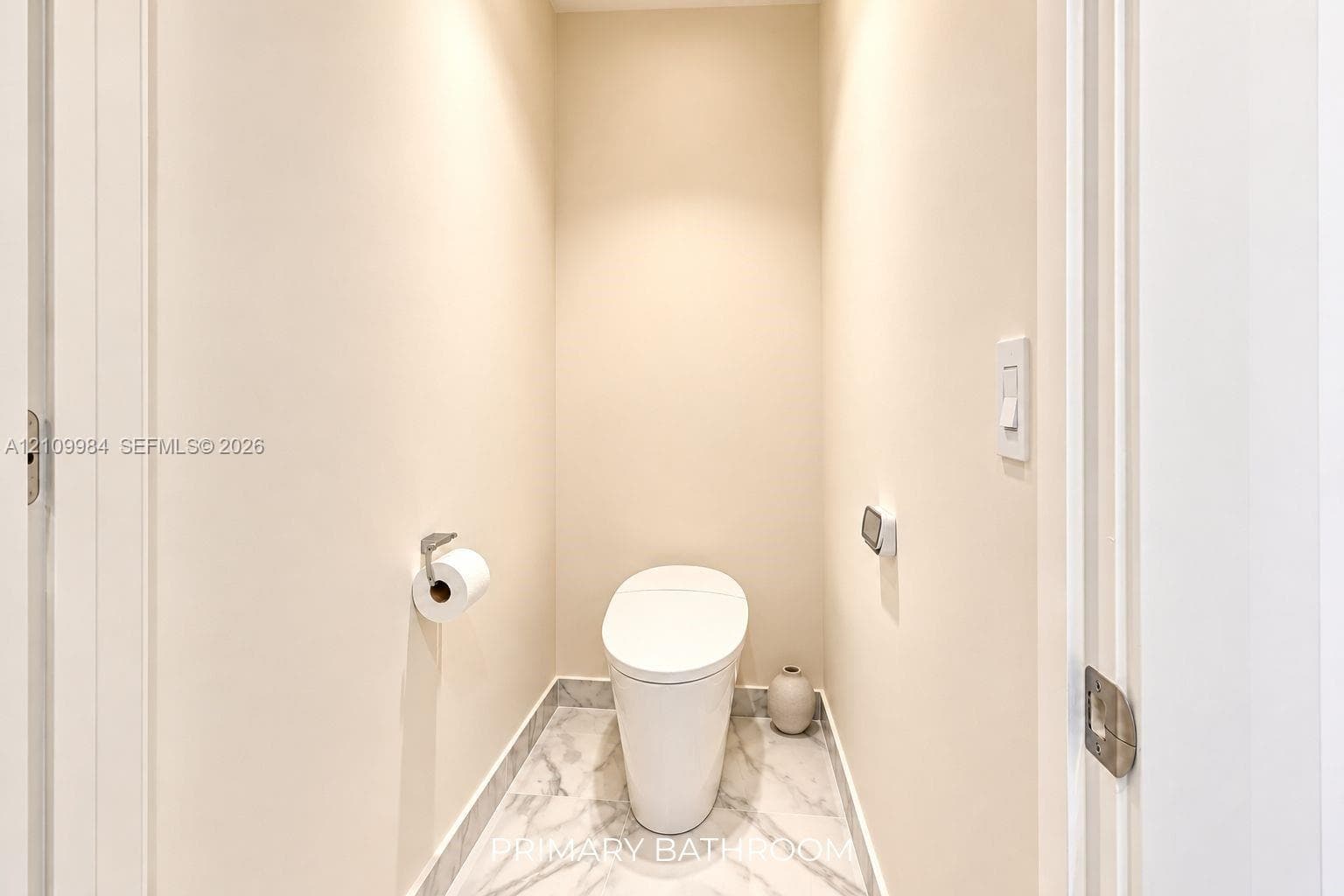 Enclosed water closet featuring a one-piece skirted toilet, large-format stone-finish floor tile, and brushed metal hardware