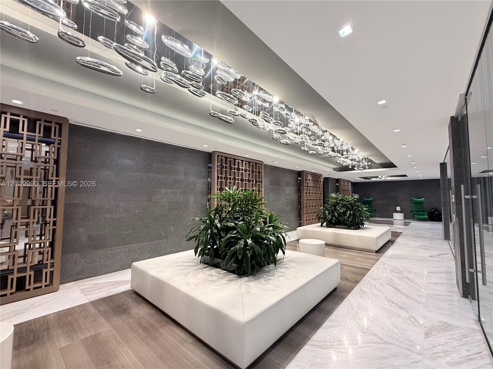 Lobby featuring stone tile flooring, geometric wood wall screens, expansive linear ceiling lighting, and built-in rectangular planters