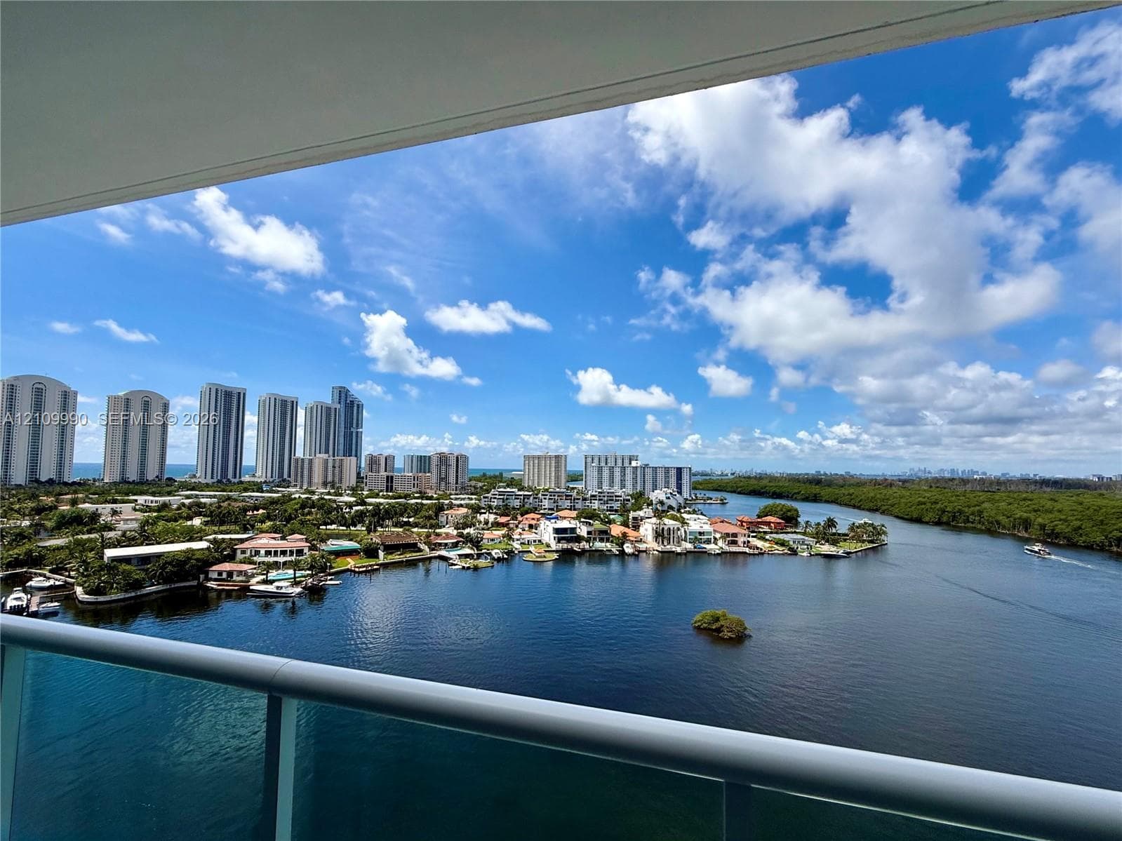 Covered balcony featuring a glass panel railing and panoramic waterway and urban skyline scenery