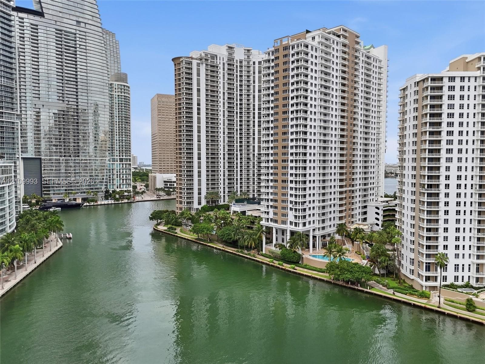 Waterfront high-rise complex featuring multiple exterior balconies, ground-level pool area, concrete bulkhead, and mature landscaping