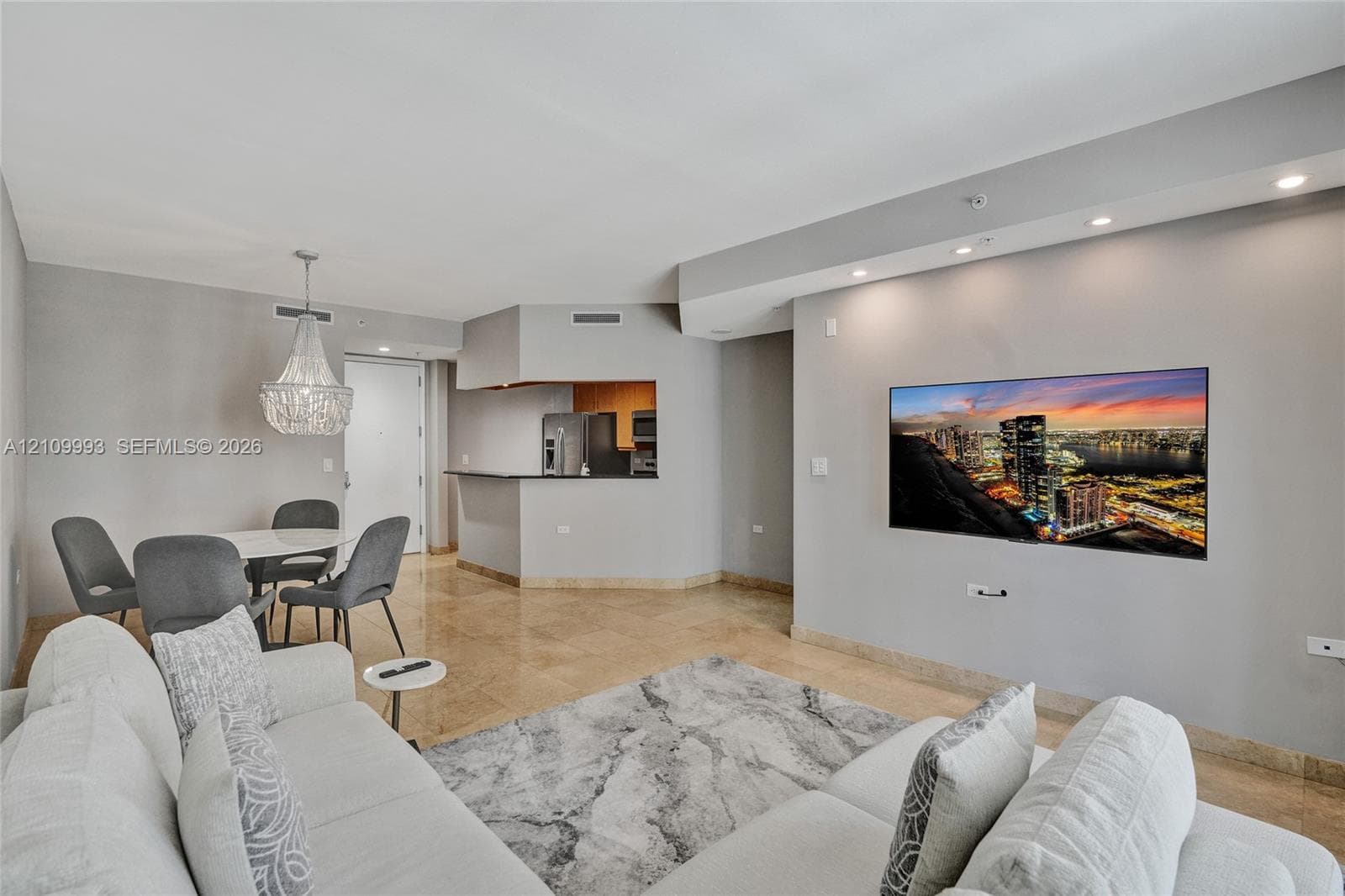 Open living area featuring polished stone flooring, recessed ceiling lighting, a crystal chandelier, and a built-in breakfast bar