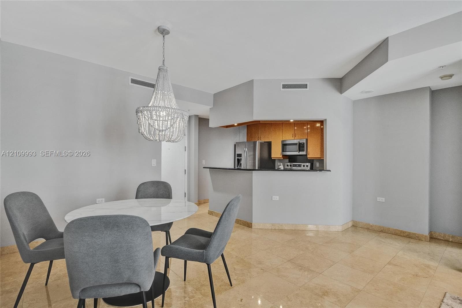 Open-concept space featuring polished natural stone flooring, decorative beaded chandelier, and kitchen pass-through with breakfast bar seating and stone countertop