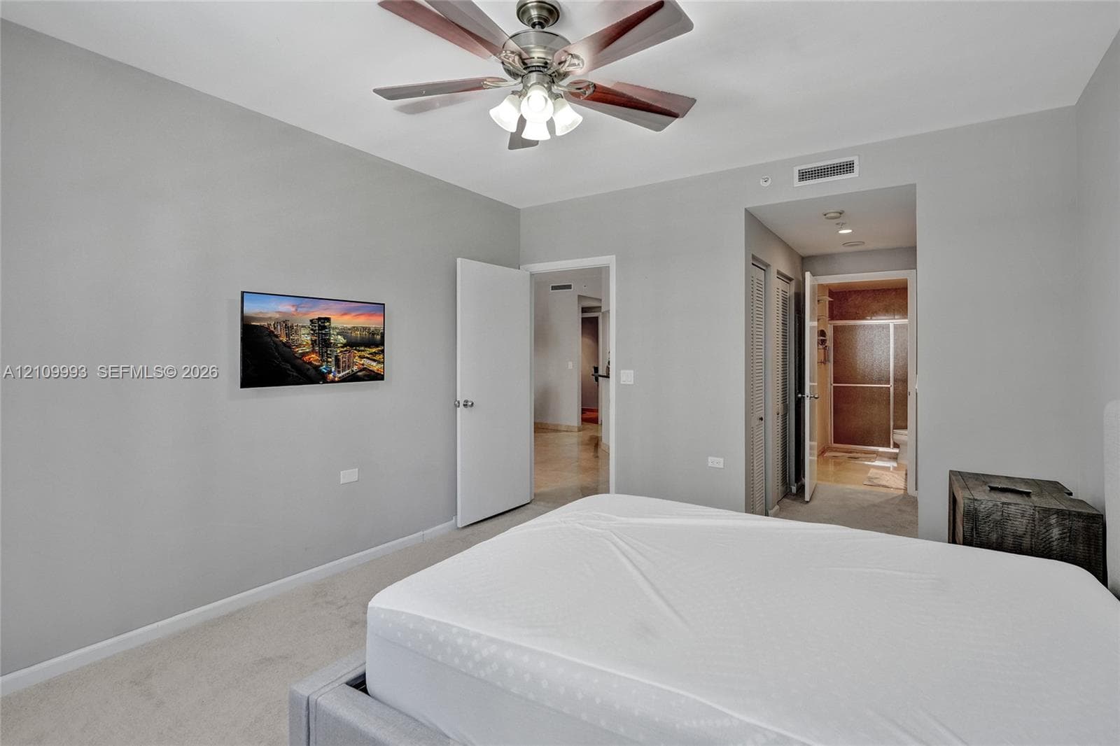 Neutral-toned interior featuring carpeting, a multi-blade ceiling fan with integrated lighting, and dual louvered closet doors