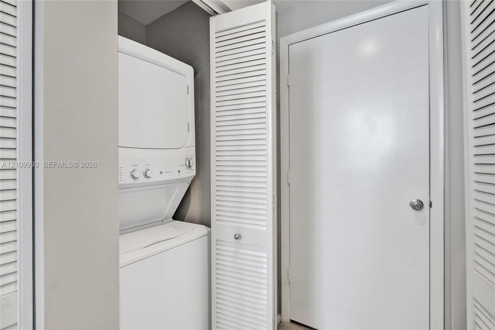 Laundry closet featuring a stackable washer and dryer unit and white louvered doors
