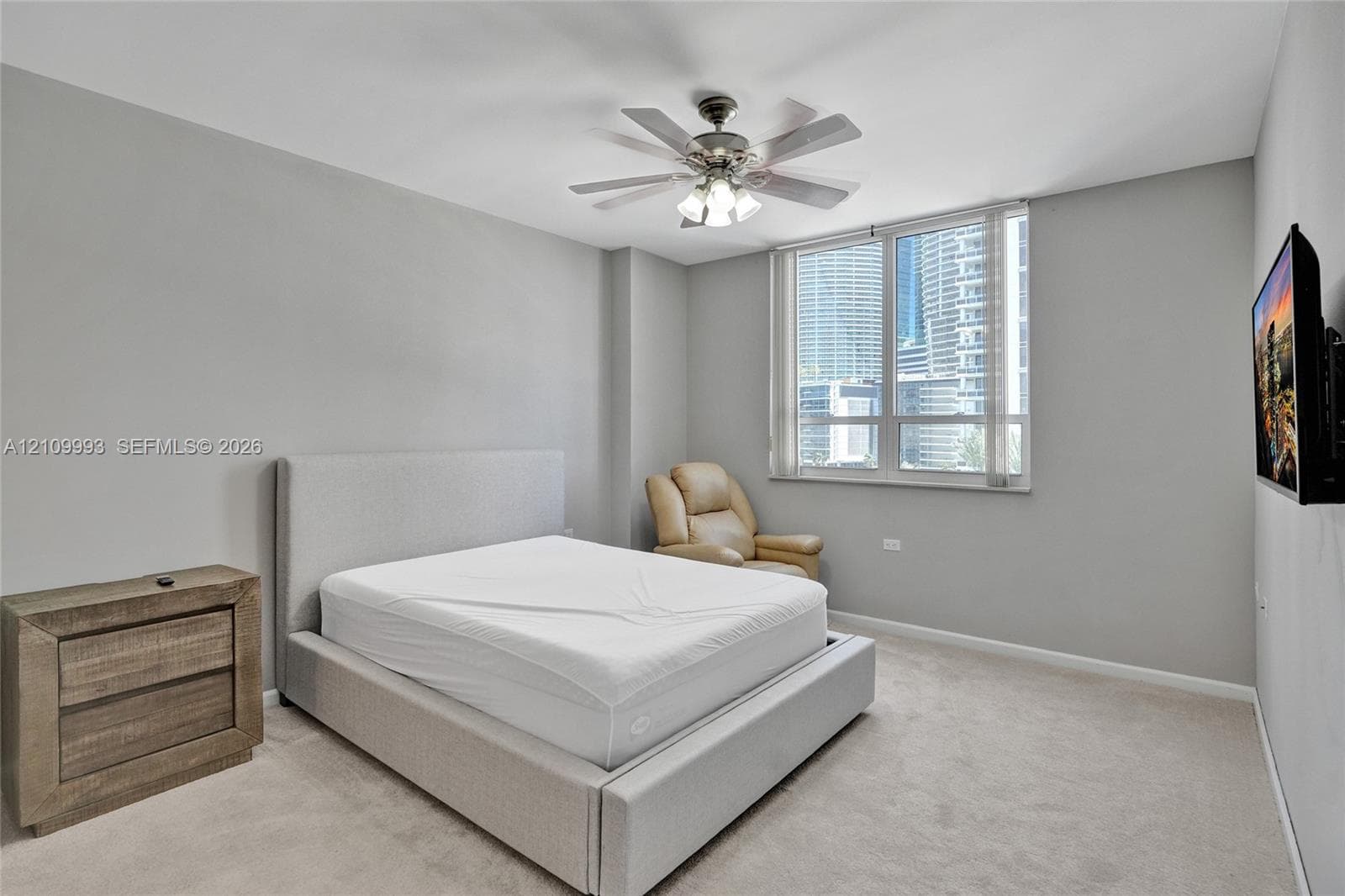 Room featuring neutral wall tones, wall-to-wall carpeting, a multi-blade ceiling fan with integrated lighting, and a large window with urban exposure