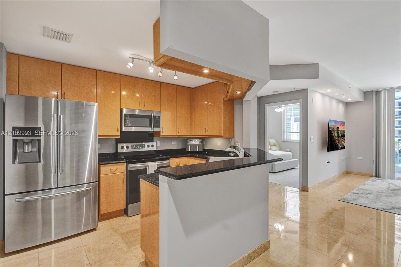 Kitchen featuring light wood-finish cabinetry, dark stone countertops, stainless steel appliances, and polished stone flooring
