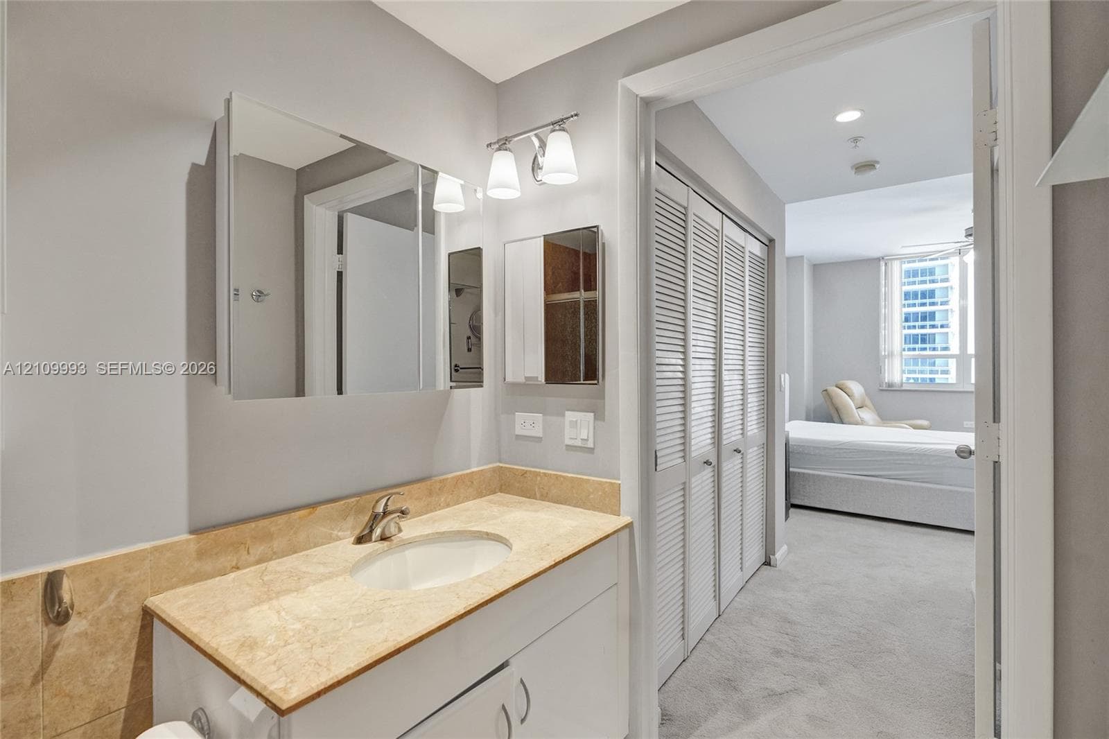 Bathroom featuring a vanity with stone-surround countertop, integrated sink, and dual-door medicine cabinet with integrated lighting