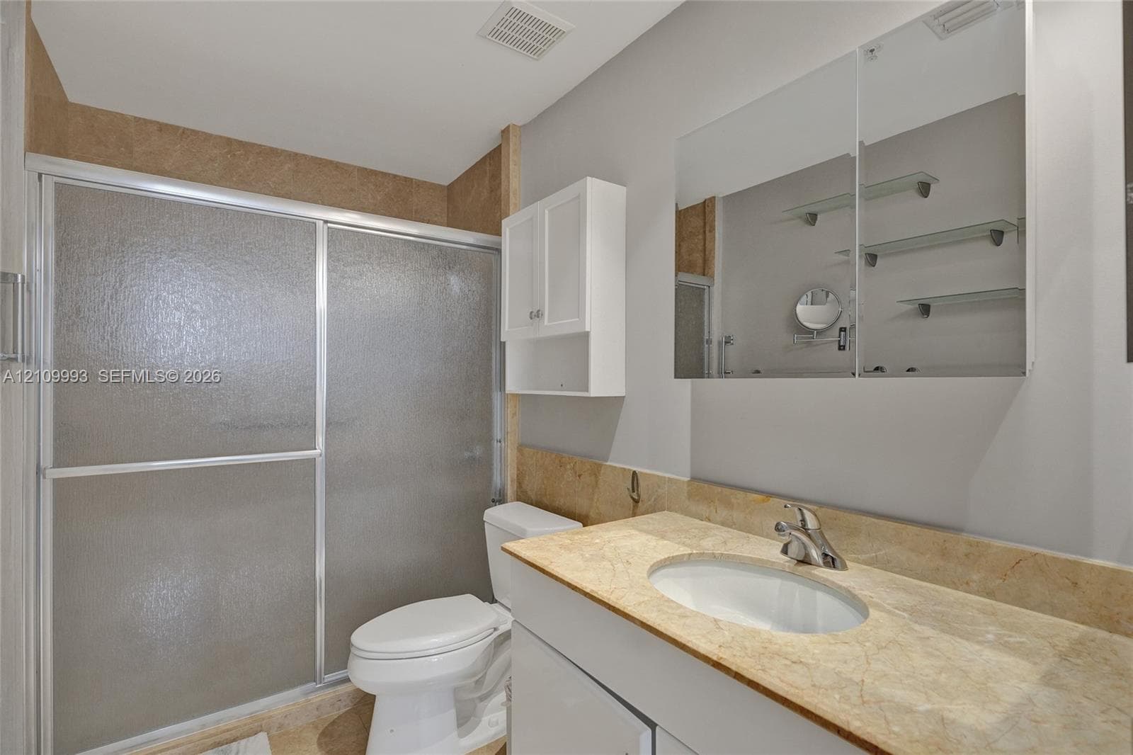 Bathroom featuring a vanity with a stone countertop, an integrated oval sink, a medicine cabinet with mirrored doors, a wall-mounted storage cabinet, and a shower with sliding glass doors