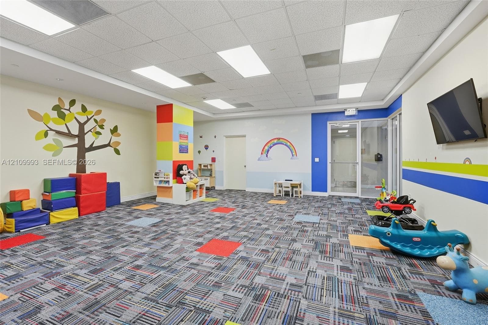 Multi-purpose room featuring patterned carpet tile flooring, drop ceiling with integrated recessed lighting, and glass-panel entry door