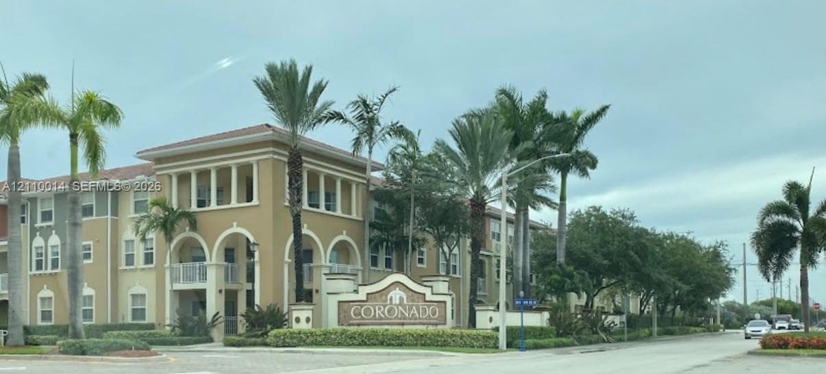 Multi-story stucco exterior featuring arched entryways, balconies with white railings, a decorative roofline, and mature palm landscaping