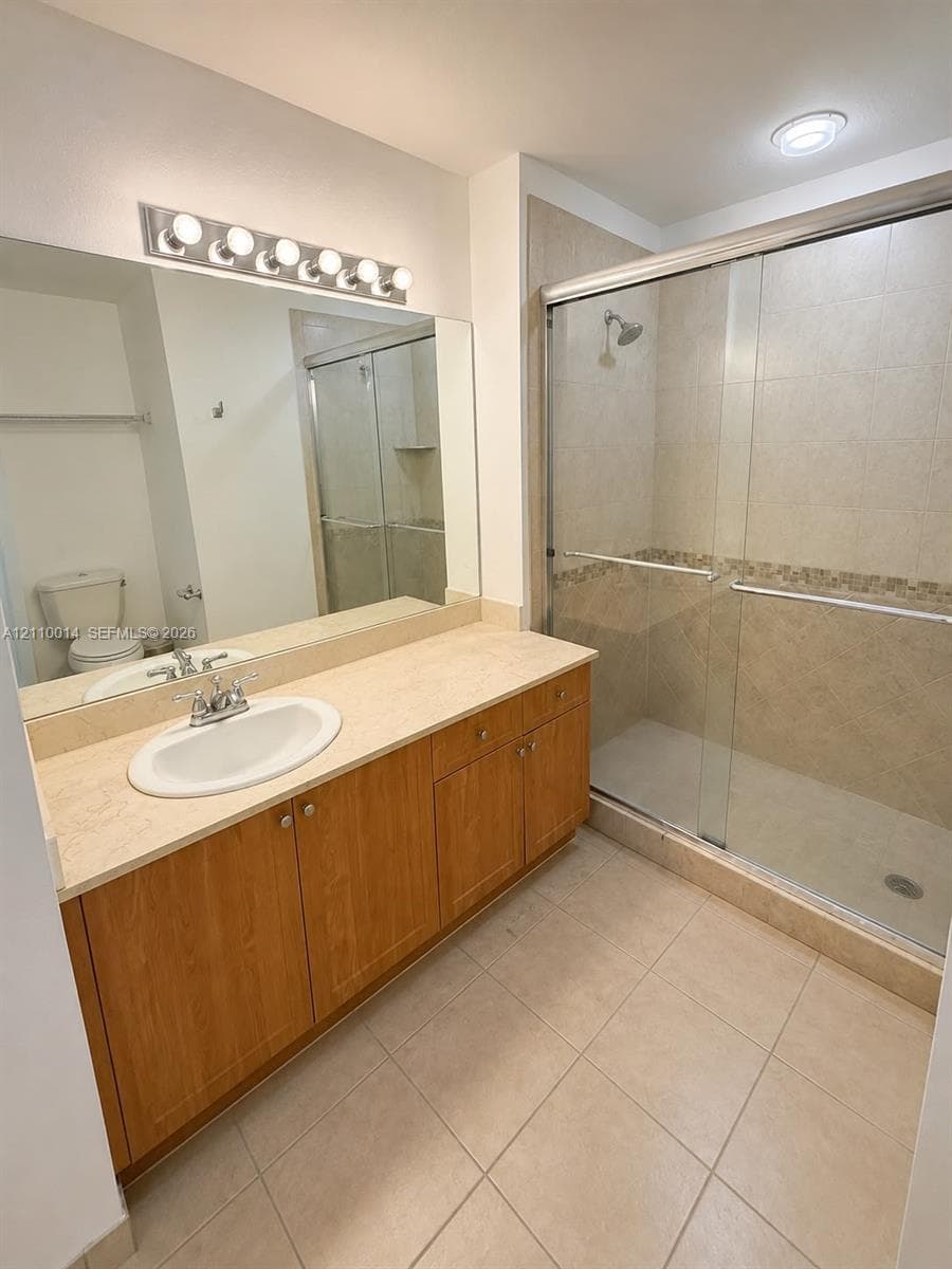 Bathroom vanity with wood-finish cabinetry, countertop with an integrated basin, expansive wall-mounted mirror, walk-in shower with glass sliding doors, and ceramic tile flooring