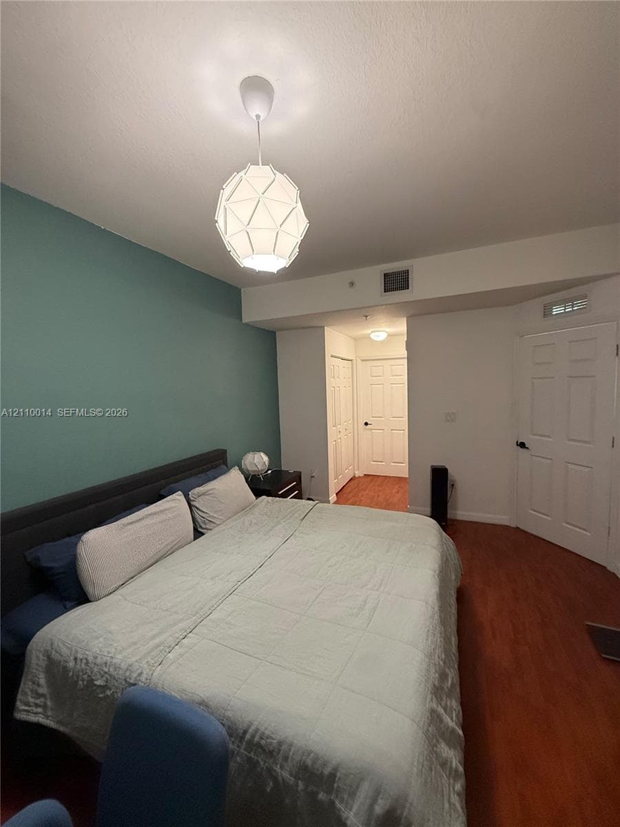 Room featuring wood-finish flooring, a geometric pendant light fixture, and a teal accent wall
