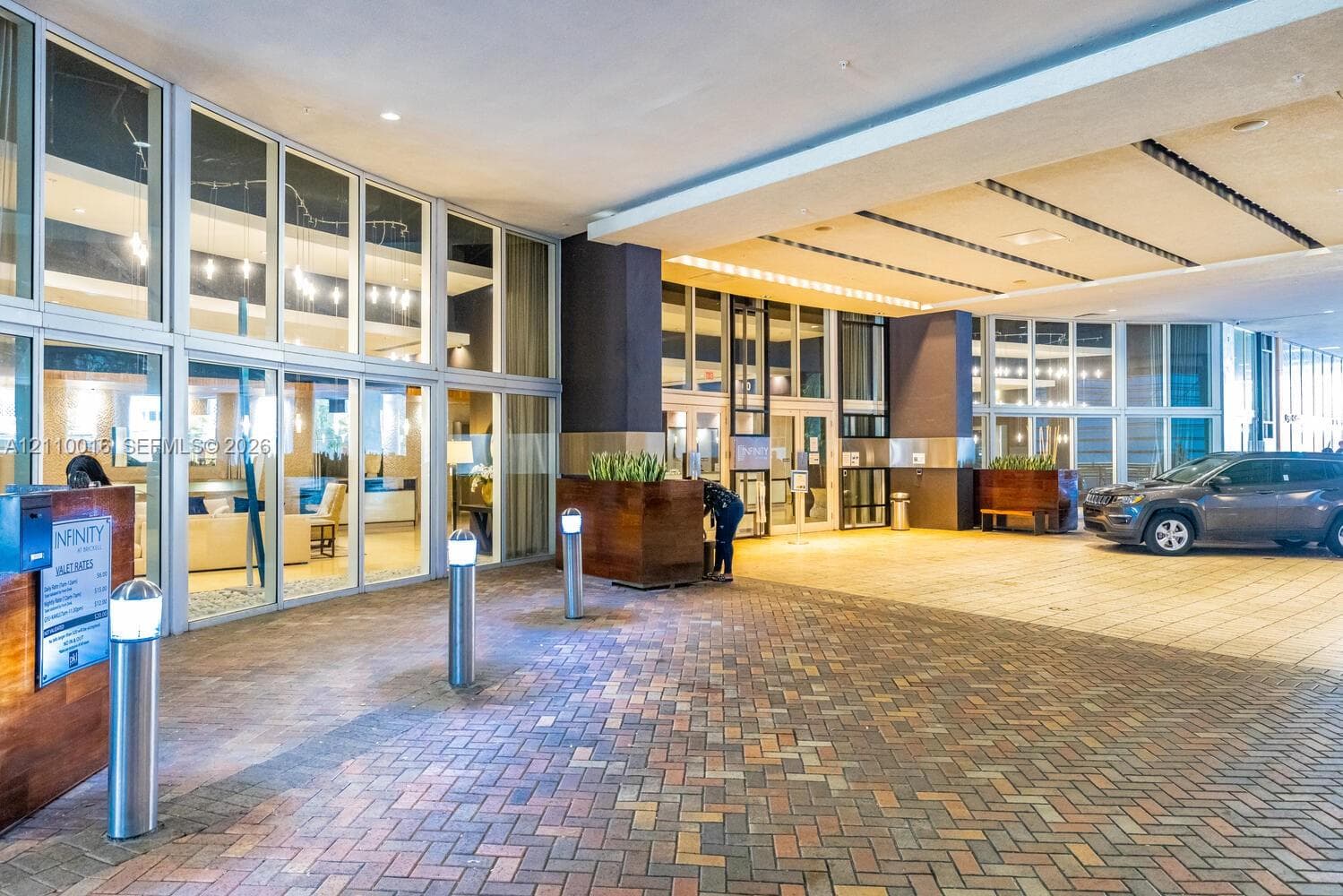 Covered entryway featuring a brick-paver drive, floor-to-ceiling glass paneling, recessed lighting, and integrated metal bollards