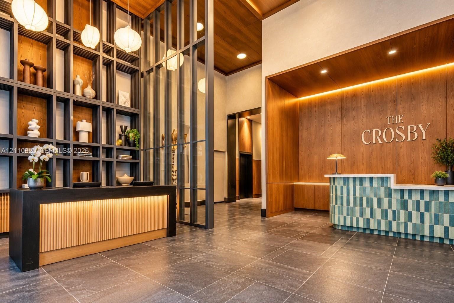 Double-height lobby featuring floor-to-ceiling grid shelving, integrated wood-paneled walls, tile-accented reception desk, and stone-finish flooring