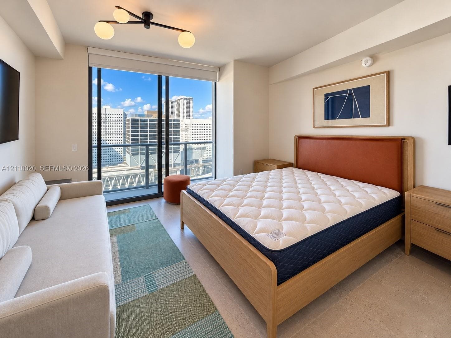 Floor-to-ceiling sliding glass door, private balcony with metal railing, modern multi-globe light fixture, and light-toned tile flooring