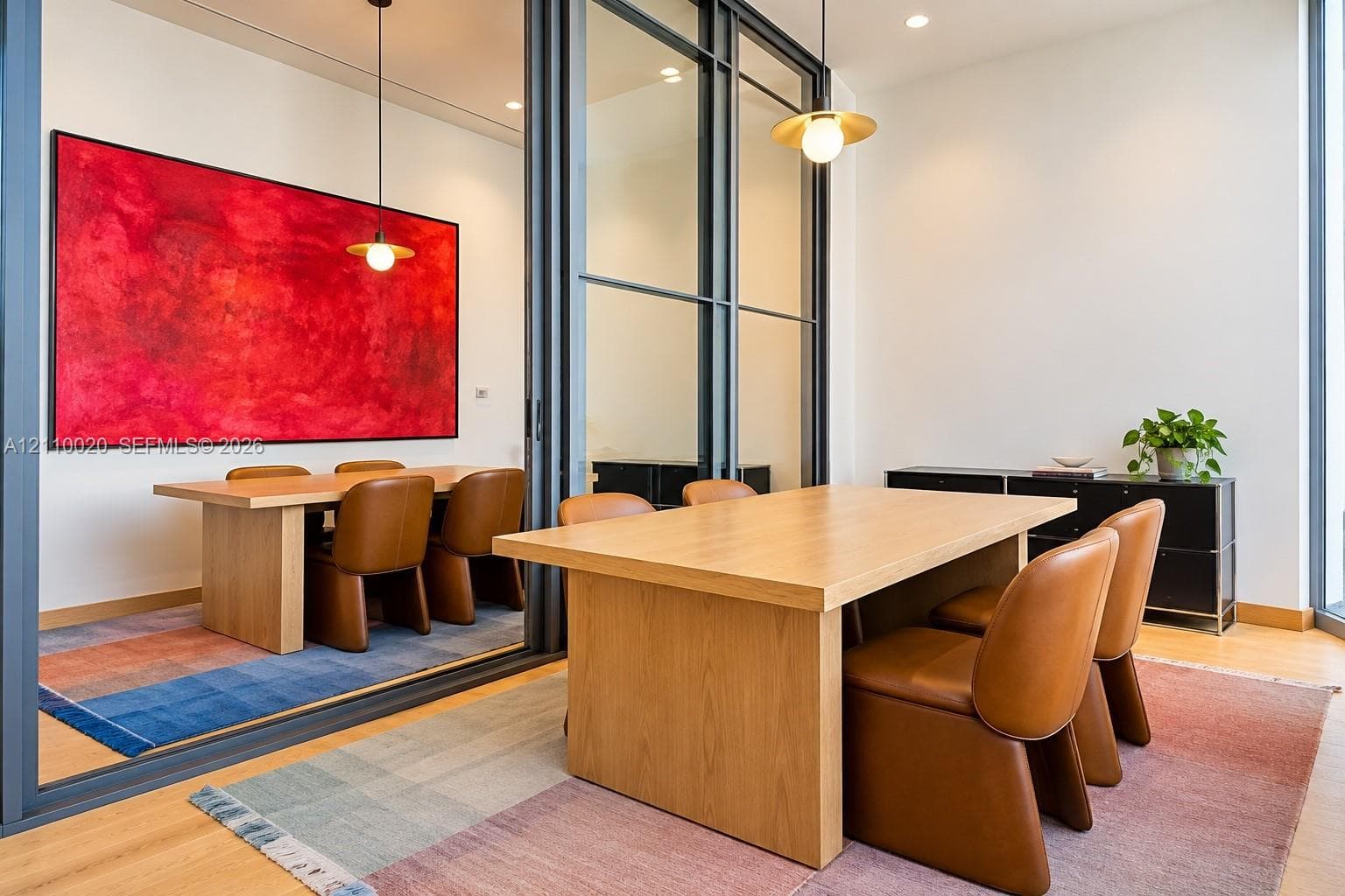 Floor-to-ceiling glass sliding partition with dark metal framing, recessed lighting, and suspended metallic pendant fixtures featuring spherical bulbs