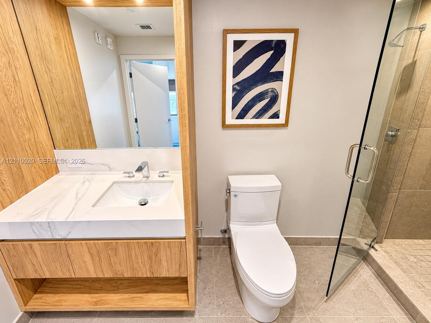 Custom wood-finish vanity with a stone-surface countertop, integrated rectangular sink, walk-in shower with a glass enclosure, and stone-tile flooring