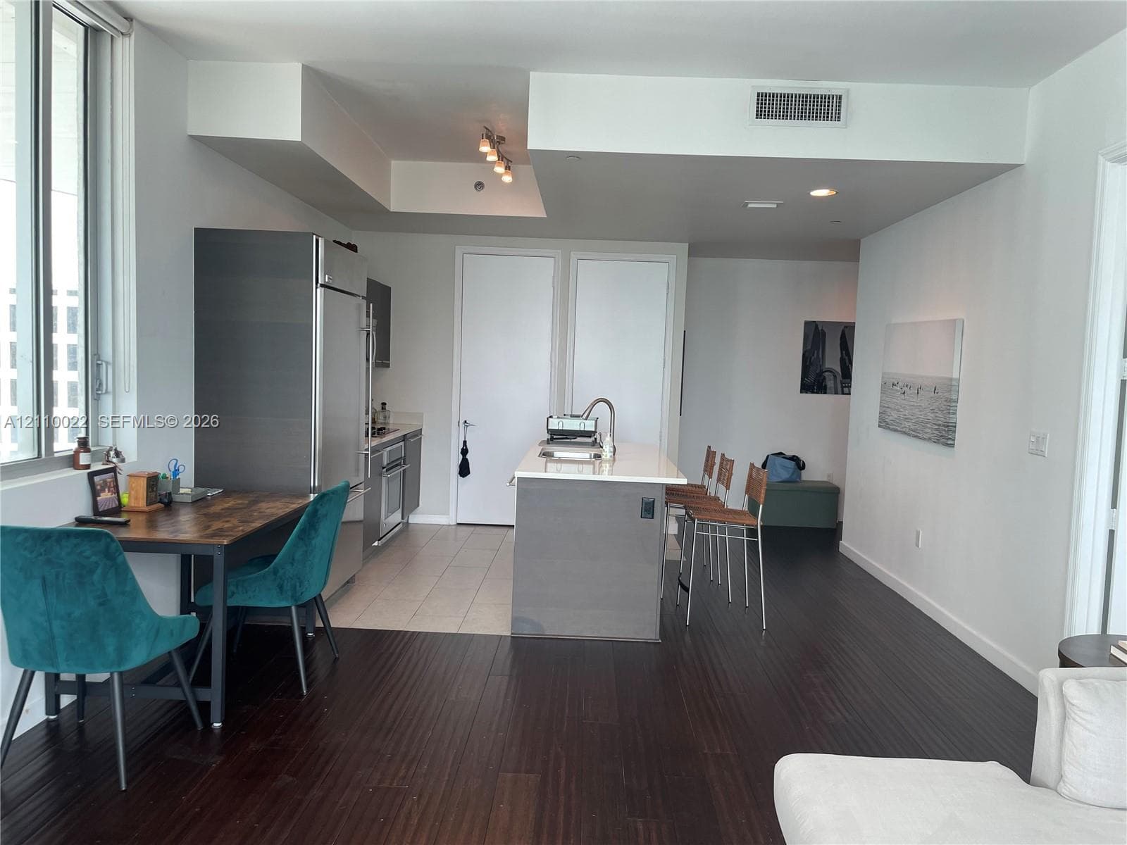 Open-concept kitchen featuring stainless steel appliances, a central island with a stone countertop, and dark wood-finish flooring